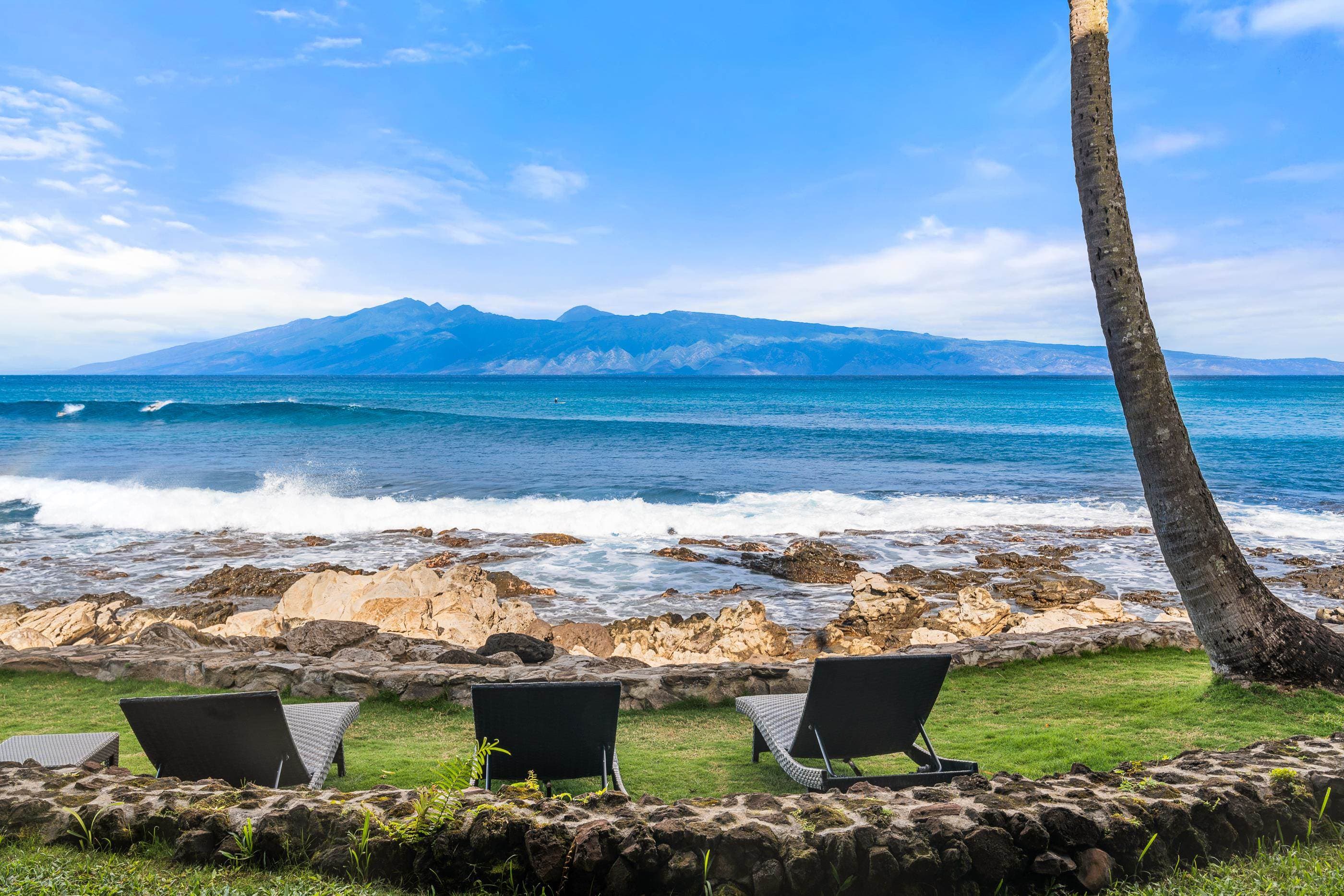 Lounge chairs on the oceanfront lawn behind the rock wall, Molokai across the water