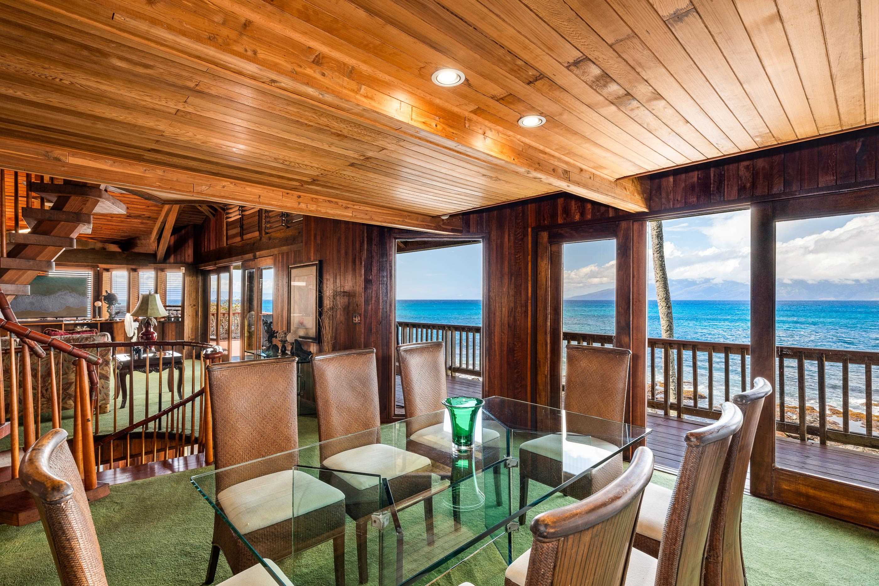 Glass dining table set beneath the open-beam ceiling, deck railing and channel view through the doors
