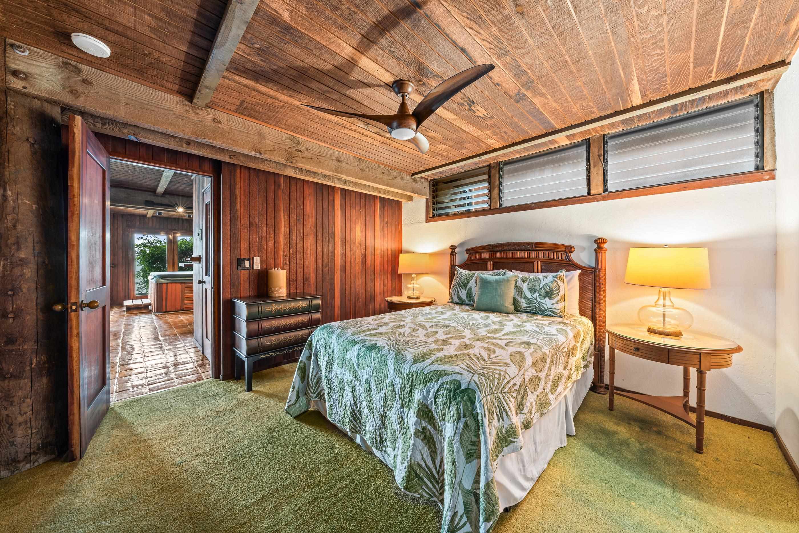 Bedroom under the planked ceiling, ceiling fan above the queen bed and louvered windows beyond