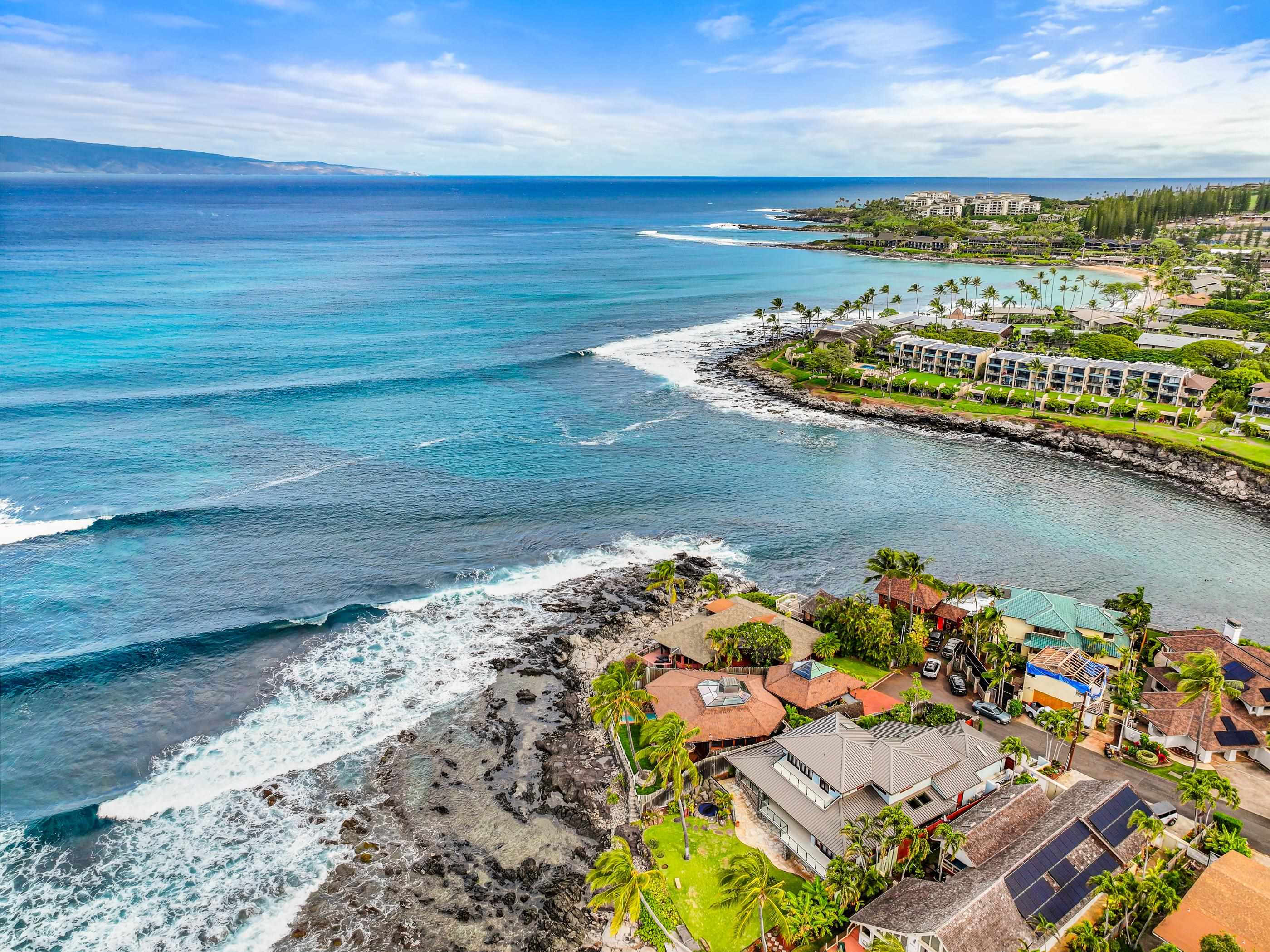 High aerial along the Napili coast: the reef arcing toward Kapalua, rooftops of the point below