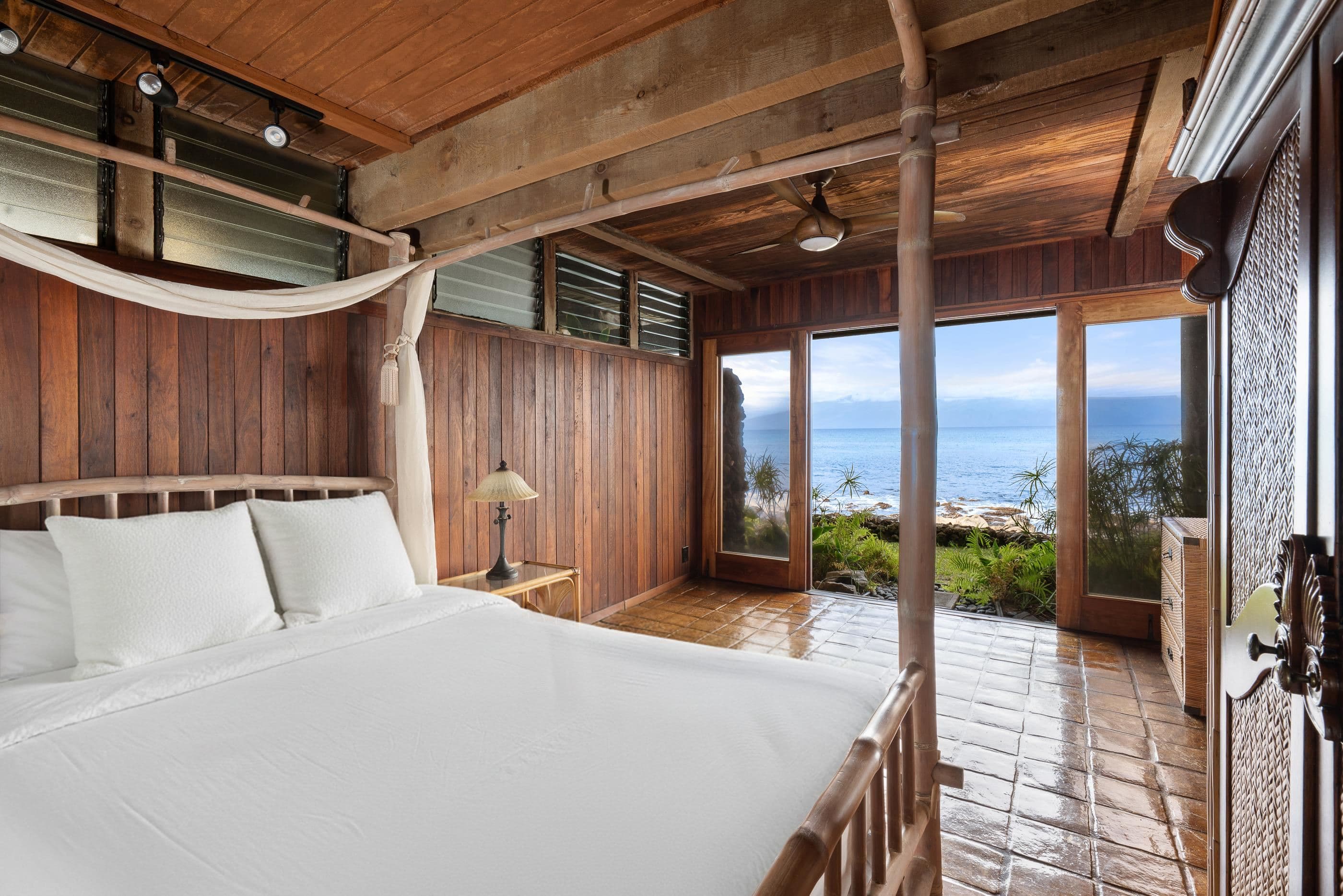 Bedroom opening straight onto the deck, netting drawn back from the bed and the channel beyond