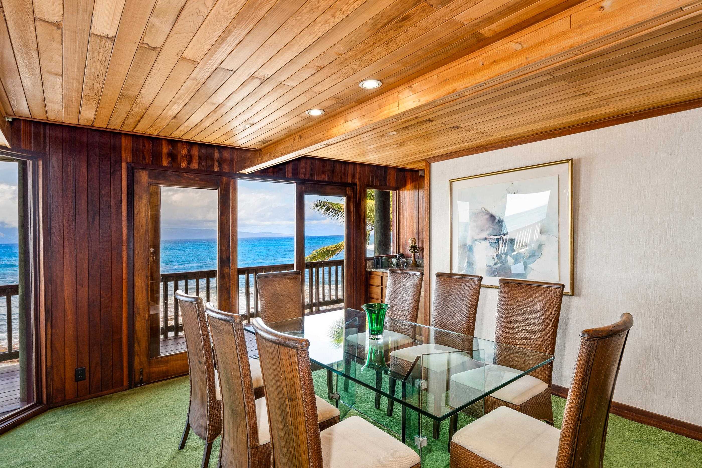 Dining area by the ocean-view windows, tall koa chairs around the glass table
