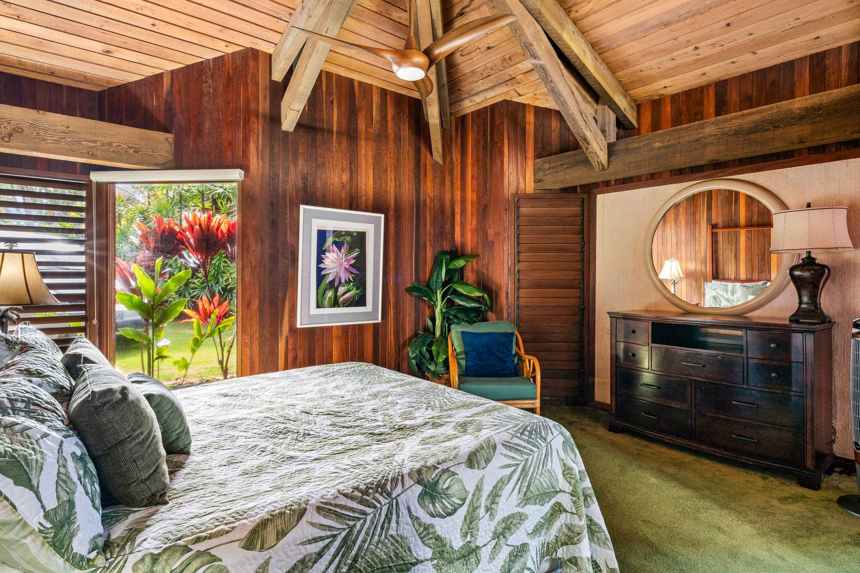 Bedroom dressed in palm-leaf linens, plants and a round mirror over the dresser